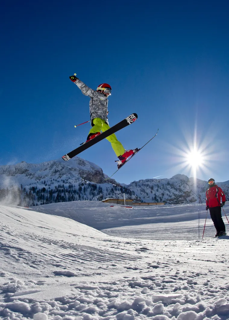 Skier jumping off snow ramp under clear blue sky in alpine ski resort